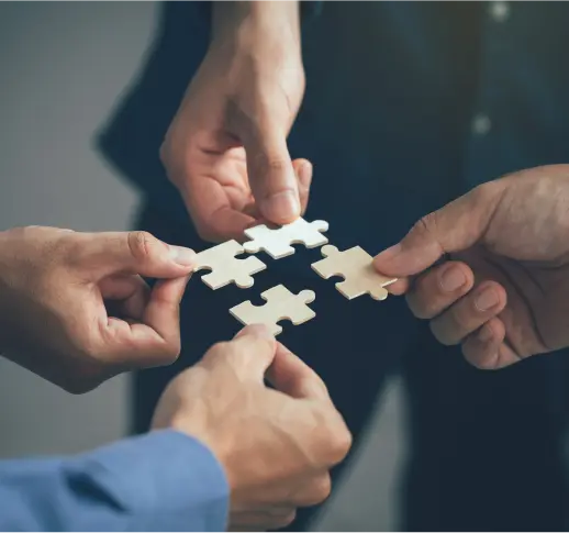 Four hands of business people connecting jigsaw puzzle pieces, symbolizing teamwork and a strategic solution.